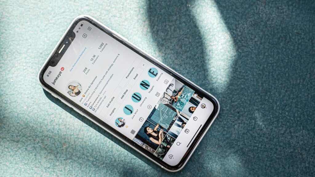 Mão segurando um smartphone em ângulo inclinado, mostrando um perfil de rede social com diversos vídeos curtos organizados na grade.