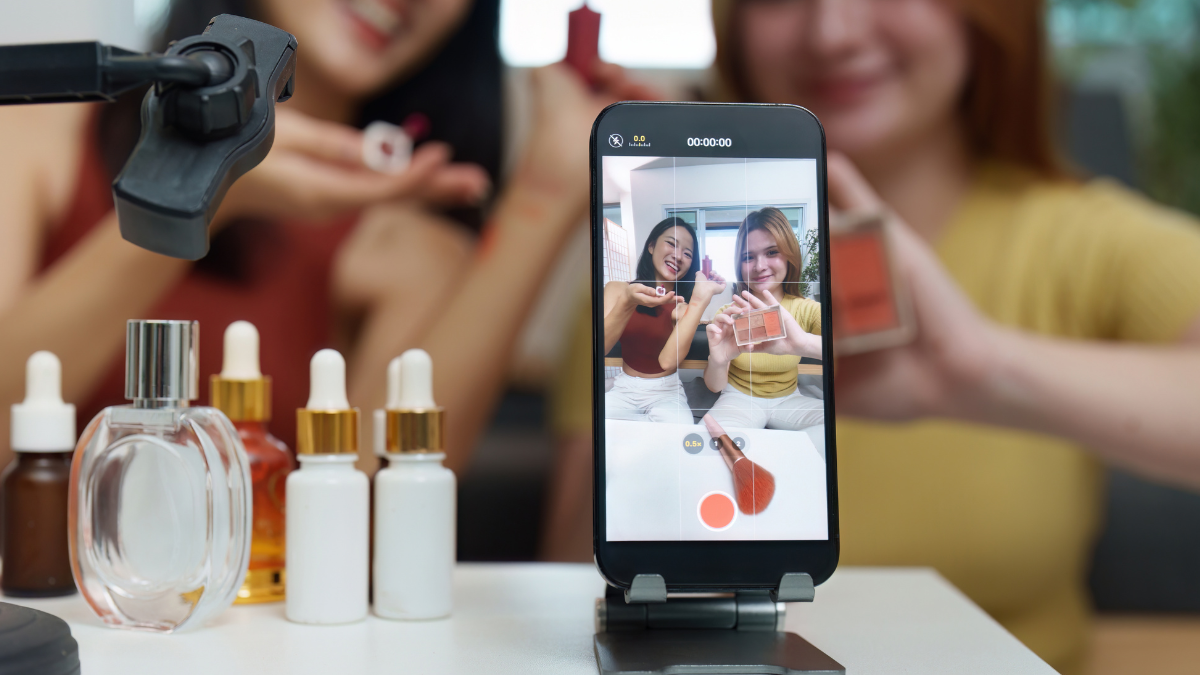 Duas mulheres produzindo conteúdo de marketing digital com smartphone e produtos de beleza sobre a mesa.